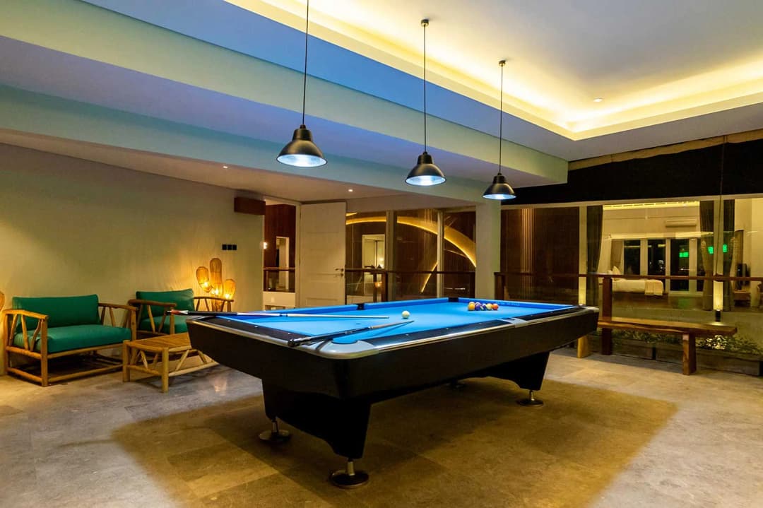 Modern indoor game room in a Bali villa featuring a professional pool table, bamboo lounge chairs, and ambient lighting.